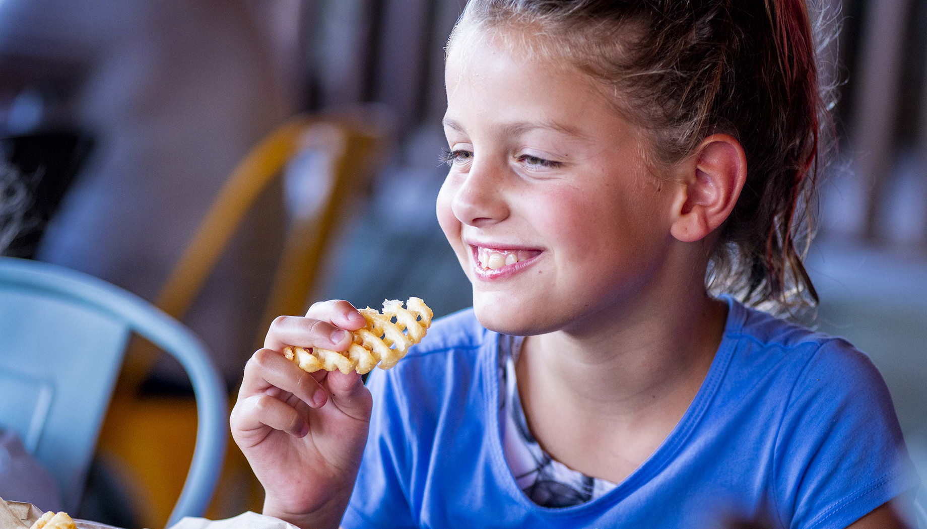 BLOG Girl in a blue shirt eating waffle fries.