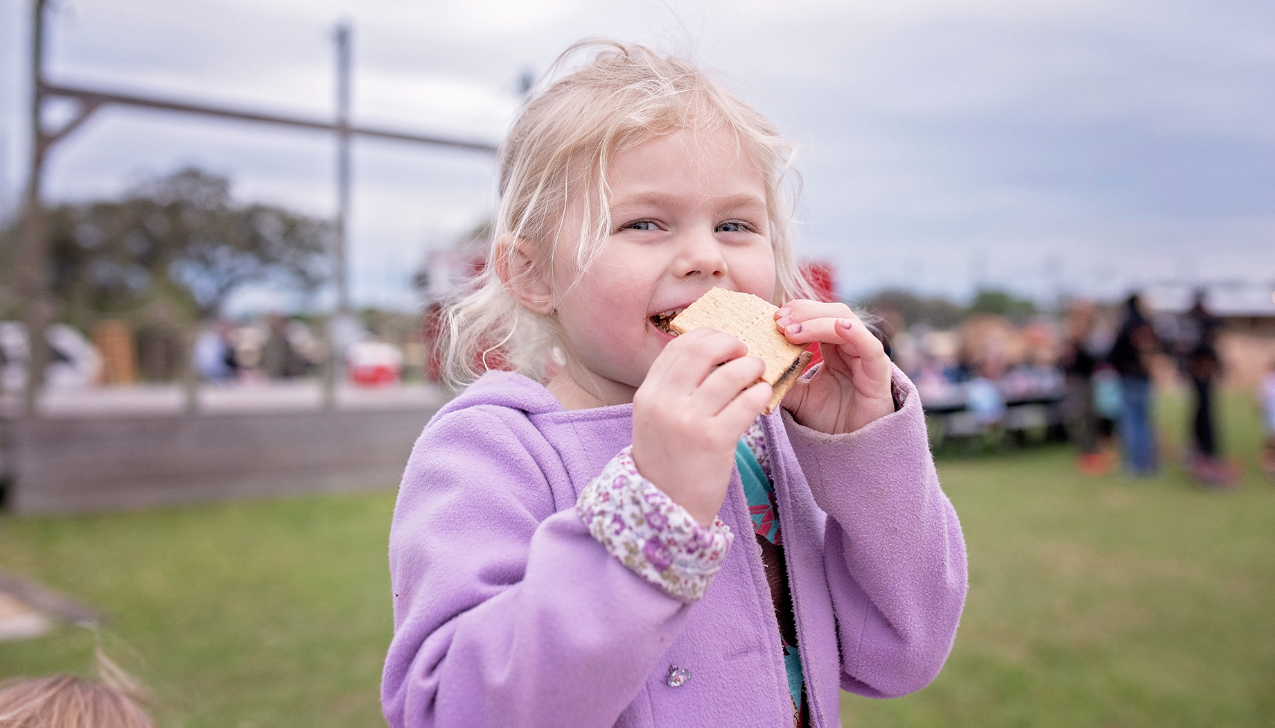 BLOG Girl in a purple jacket eating a smores.