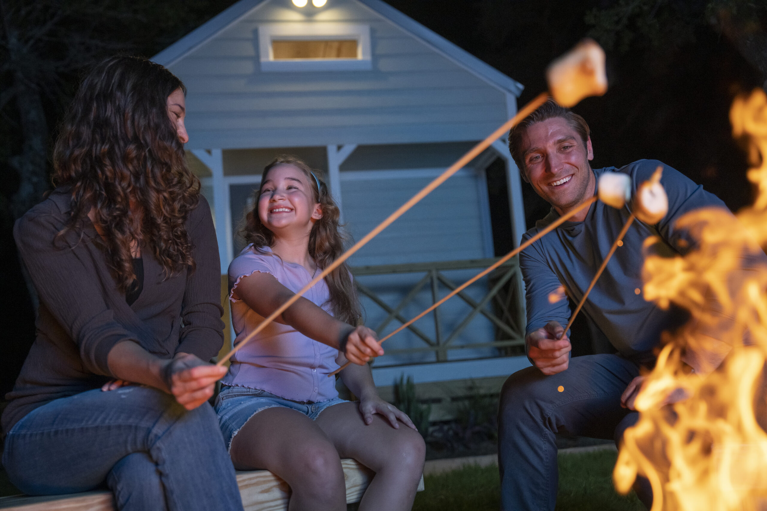 DSC03672 Family toasting marshmallows over a campfire with a cabin in the background.